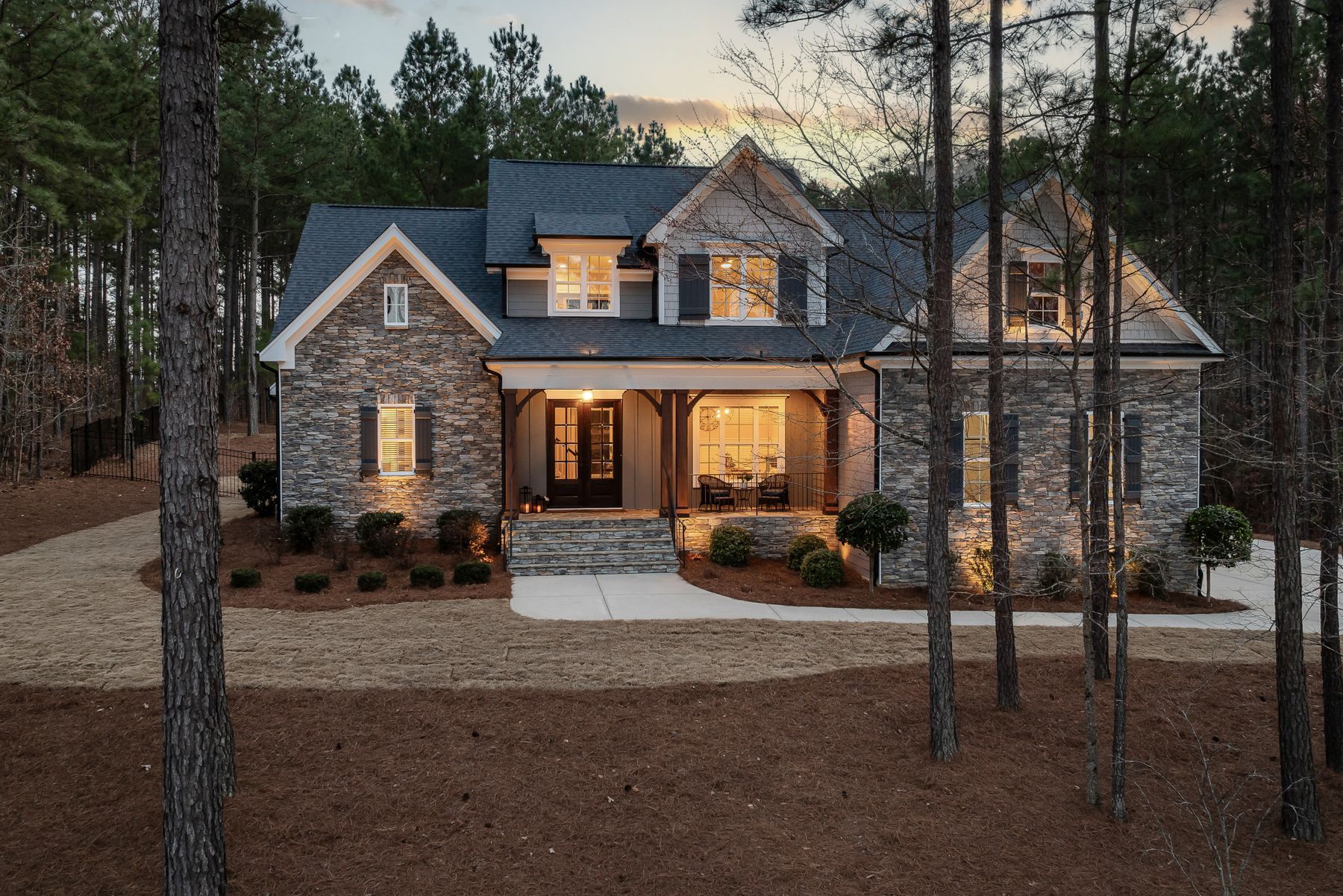 Stone and siding craftsman home at dusk with warm lights on